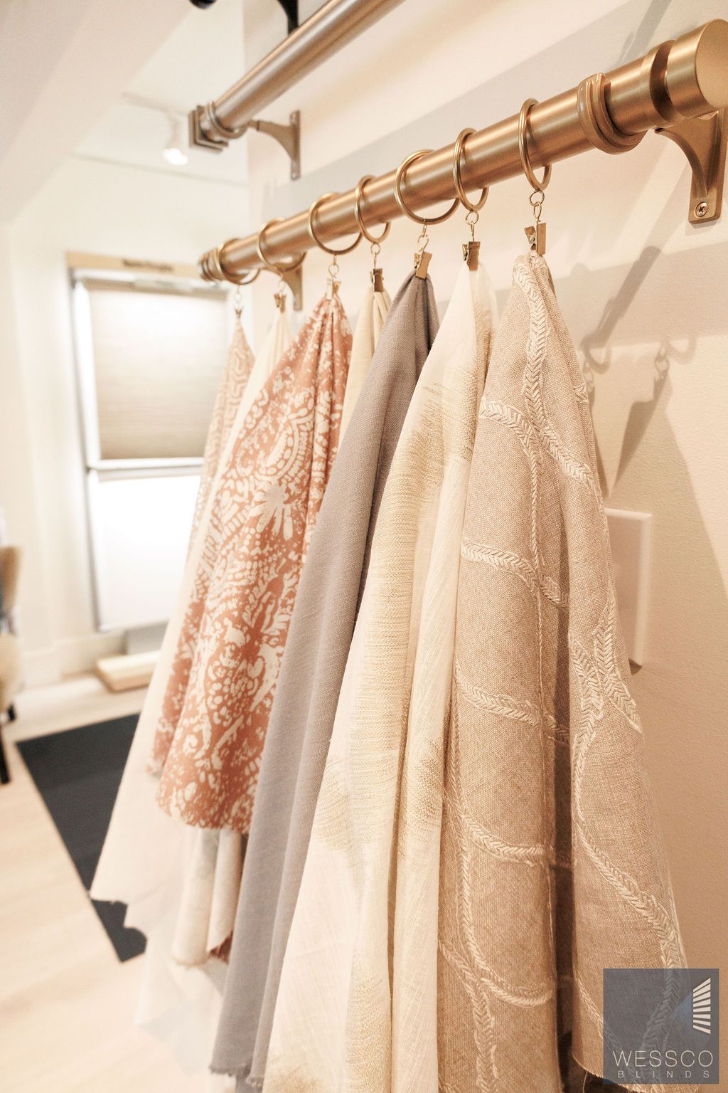 Fabric swatches hung on a gold curtain rod, showcasing various textures and colors.