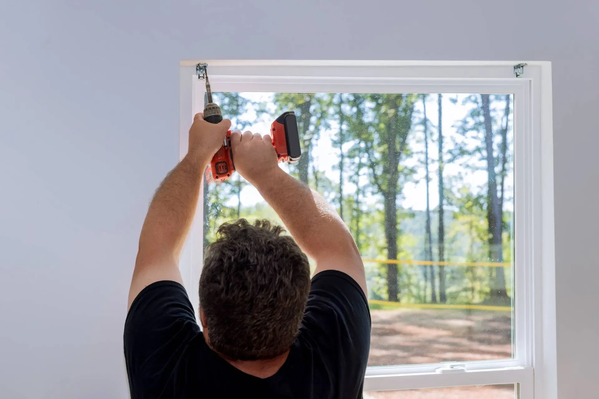 Professional window treatment installer drilling fasteners to a window frame for new blinds or shade