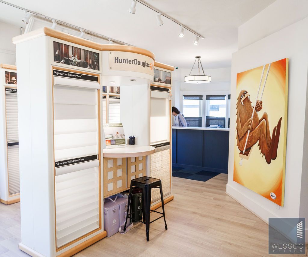 Interior of a window covering showroom, featuring displays, a painting, and a person at the desk.
