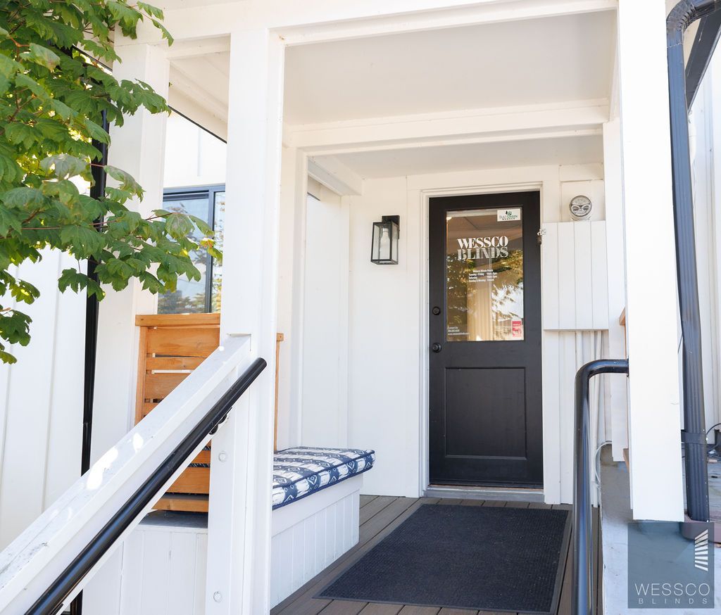 White building entrance with black door, a bench, and a welcome mat.