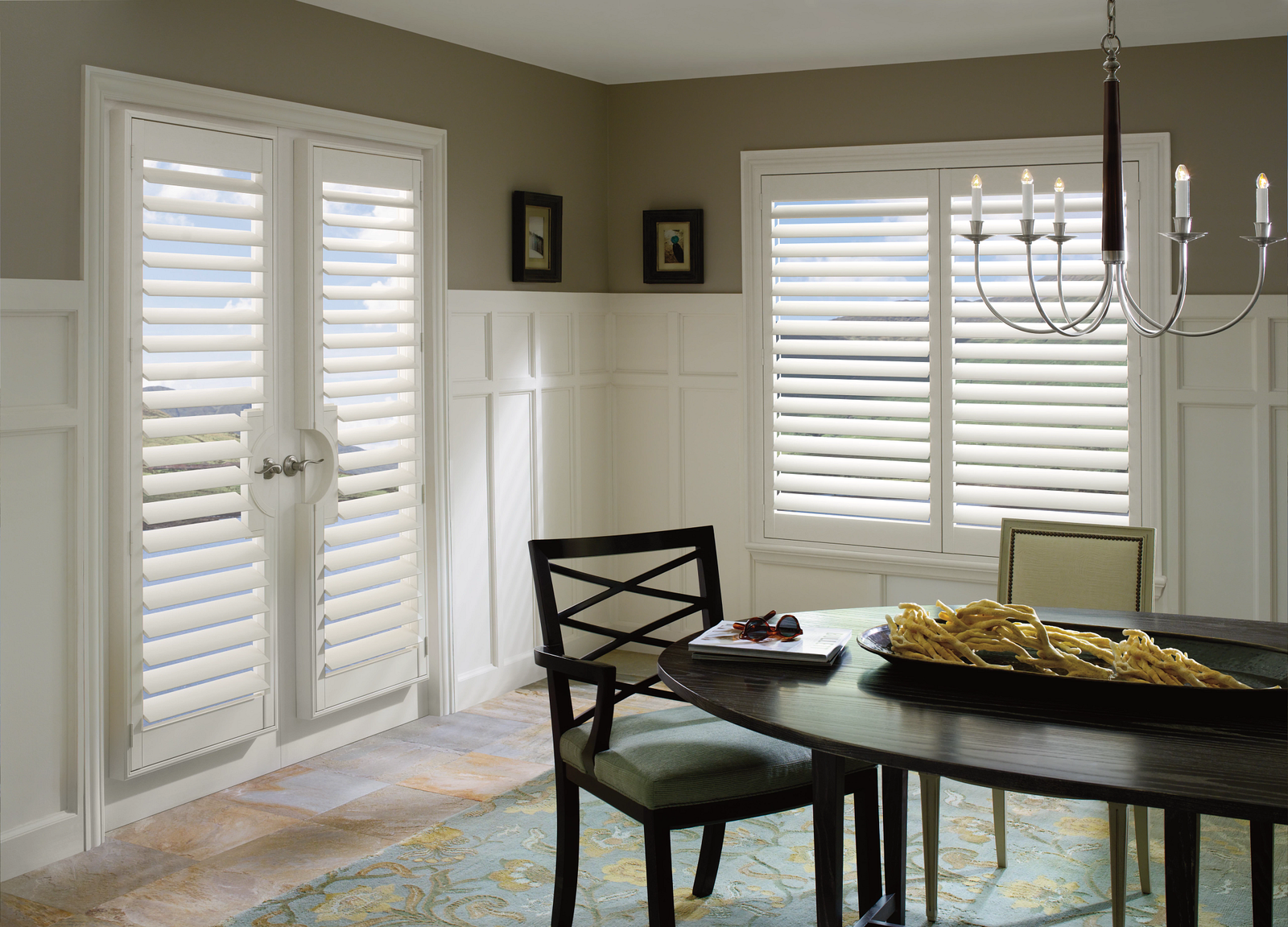 Dining room with white shutters, dark wood table, and black chairs. Light-colored walls and rug.