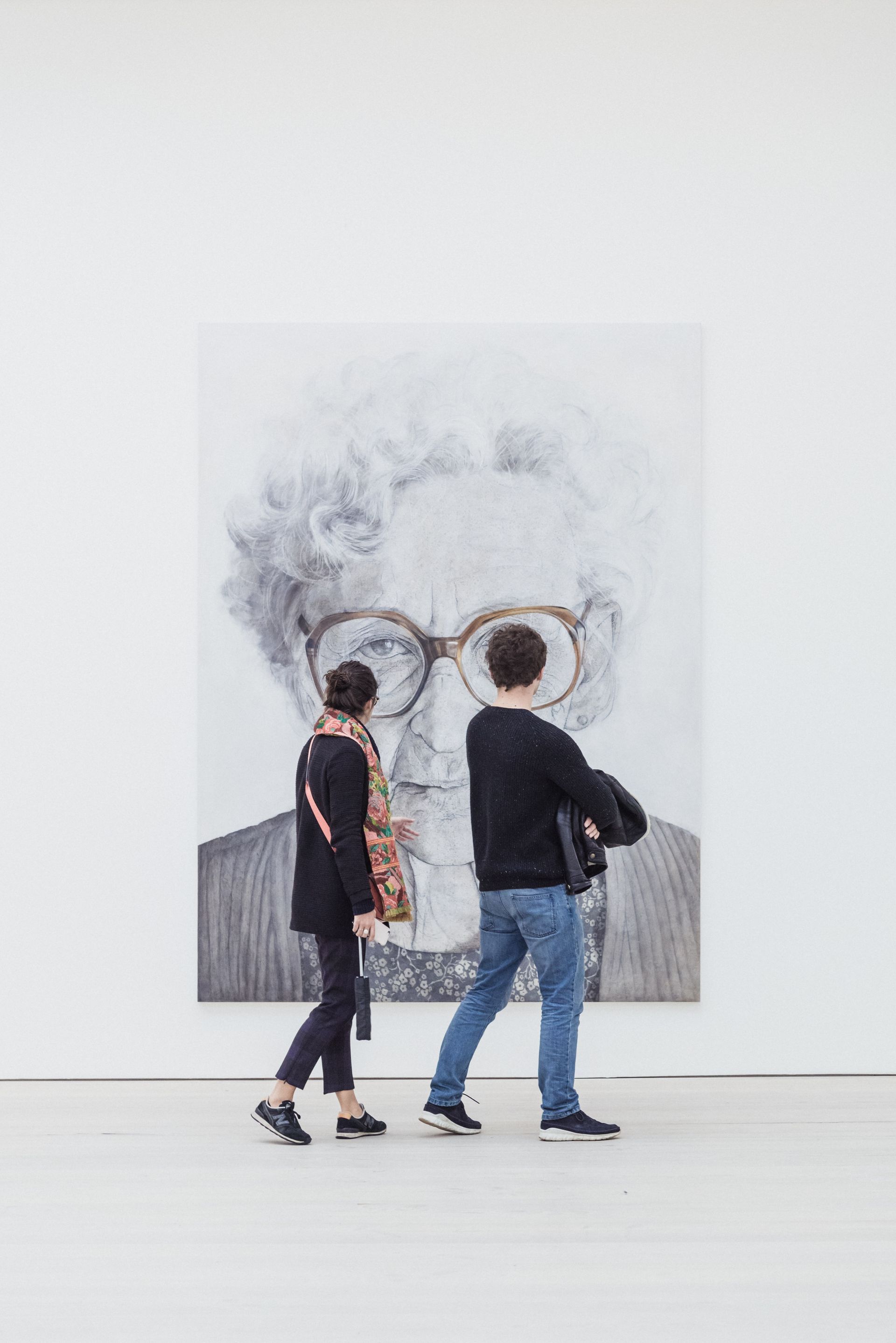 Two people view a large black and white portrait in a gallery.