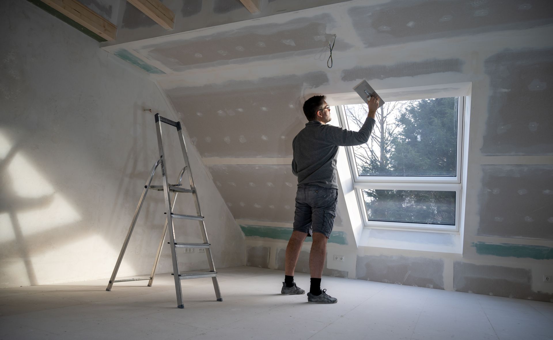 A man is standing in a room with a ladder and a window.