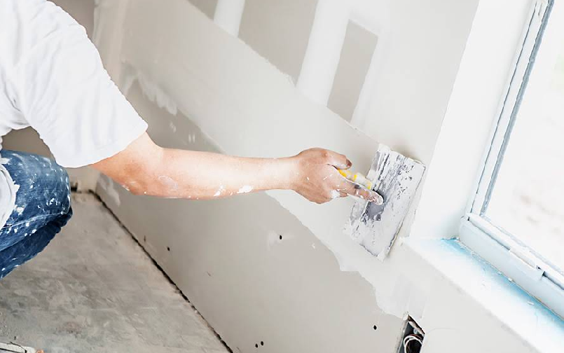 A man is kneeling down and plastering a wall. A man is kneeling down and plastering a wall.