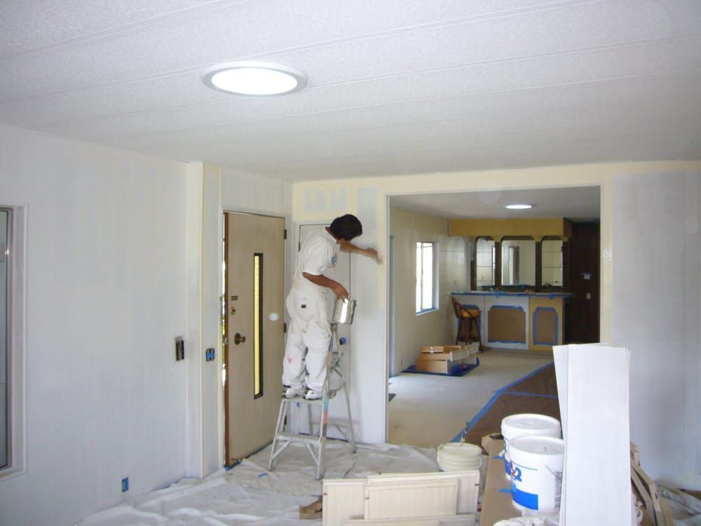 A man on a ladder paints a wall in a living room A man on a ladder paints a wall in a living room