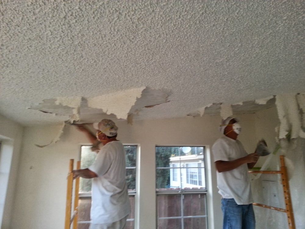 Two men wearing masks are working on a ceiling