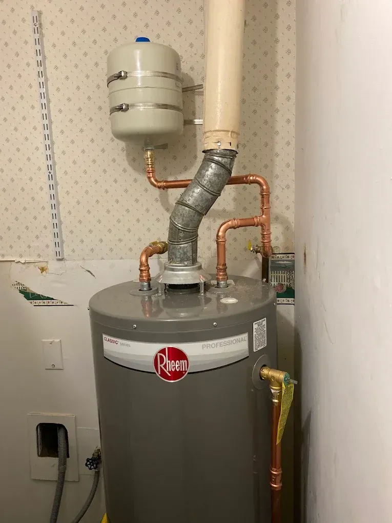 Water heater with an expansion tank, copper pipes, and vent pipe in a utility room.