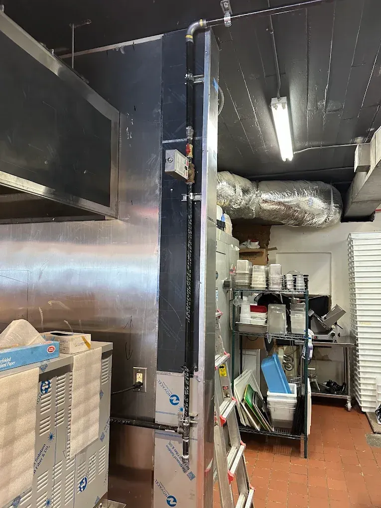 Commercial kitchen: Stainless steel hood, equipment, tall black ventilation shaft.