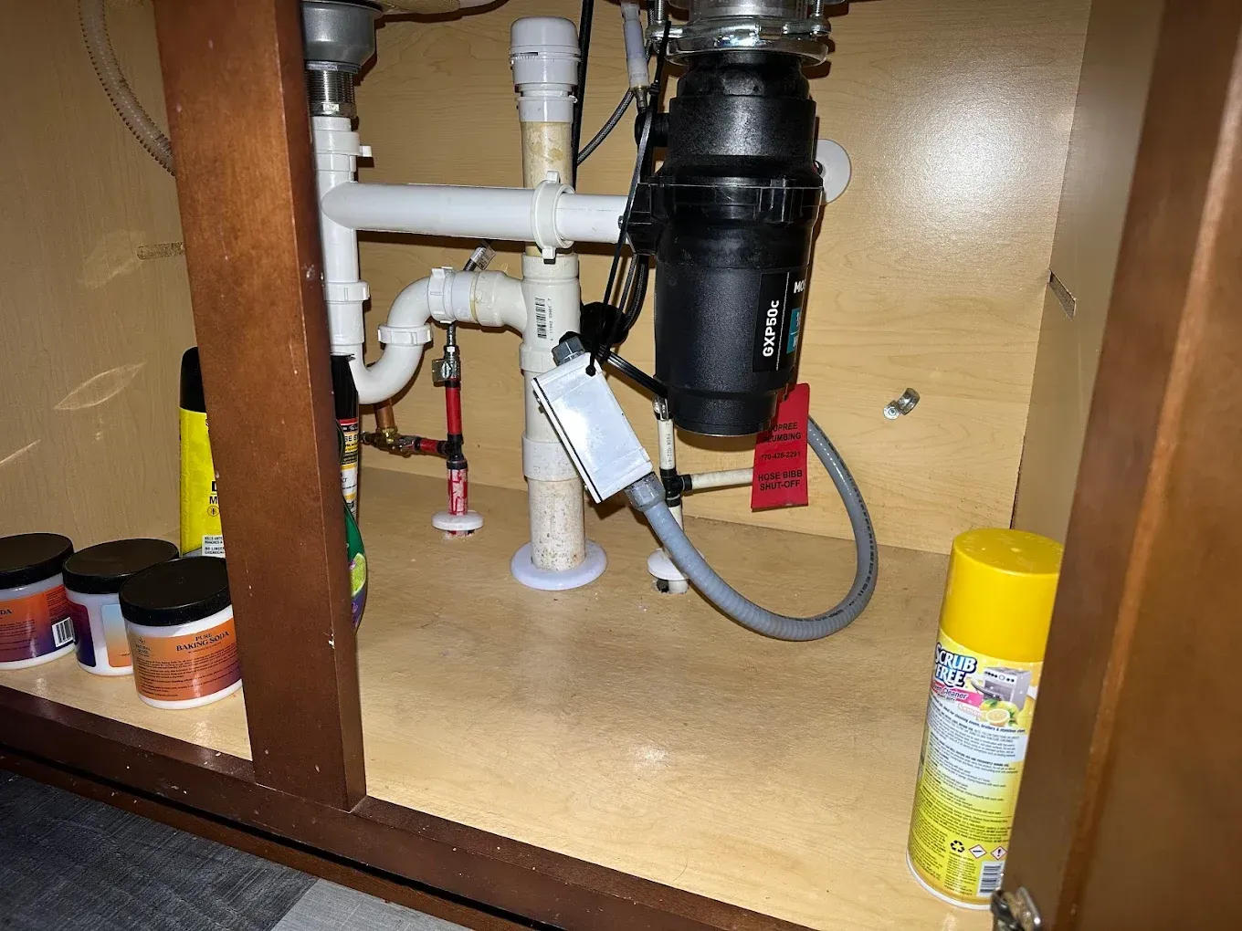 Under-sink plumbing: disposal, pipes, and connections inside a brown cabinet.