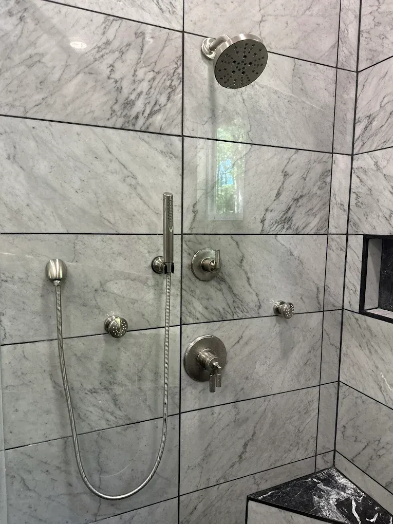 Shower with marble-look tile and brushed nickel fixtures, including a rain shower head and hand shower.