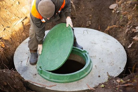 A worker installs a sewer manhole on a septic tank made of concrete rings. Construction of sewerage networks for country houses