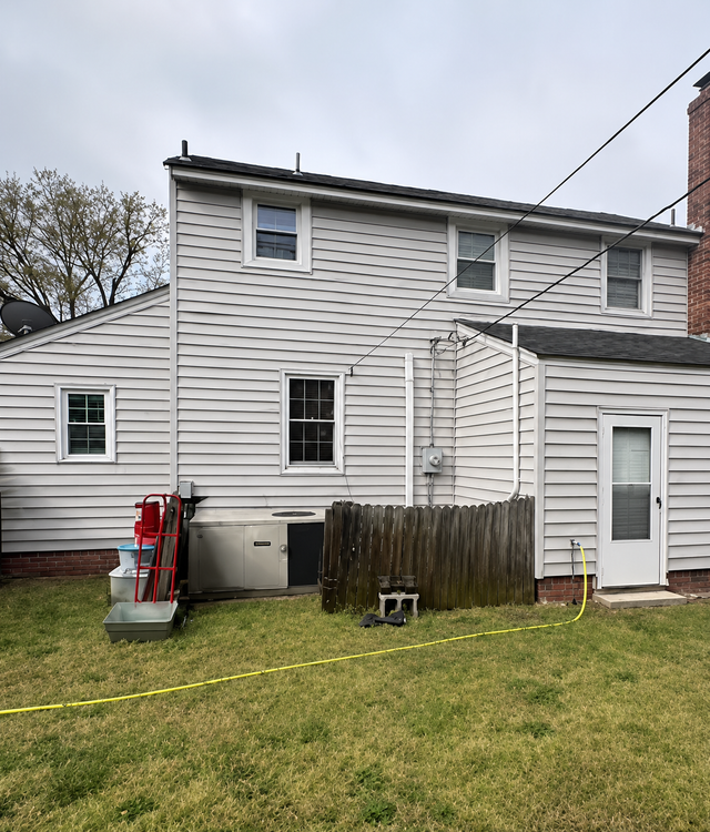 Backyard view of a gray two-story house with white trim, small windows, and a fenced patio area