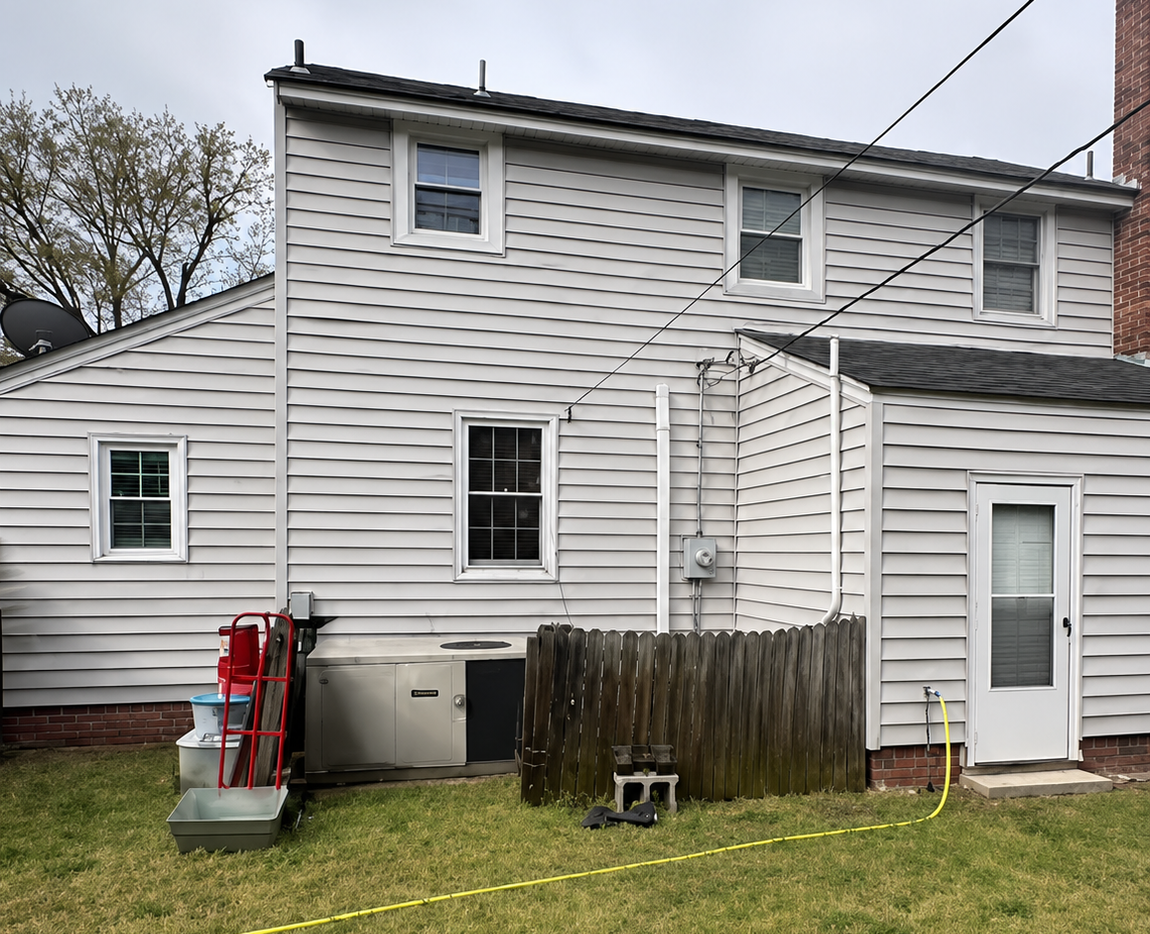Back of a white house with a small fenced yard, deck stairs, and red outdoor equipment on the left