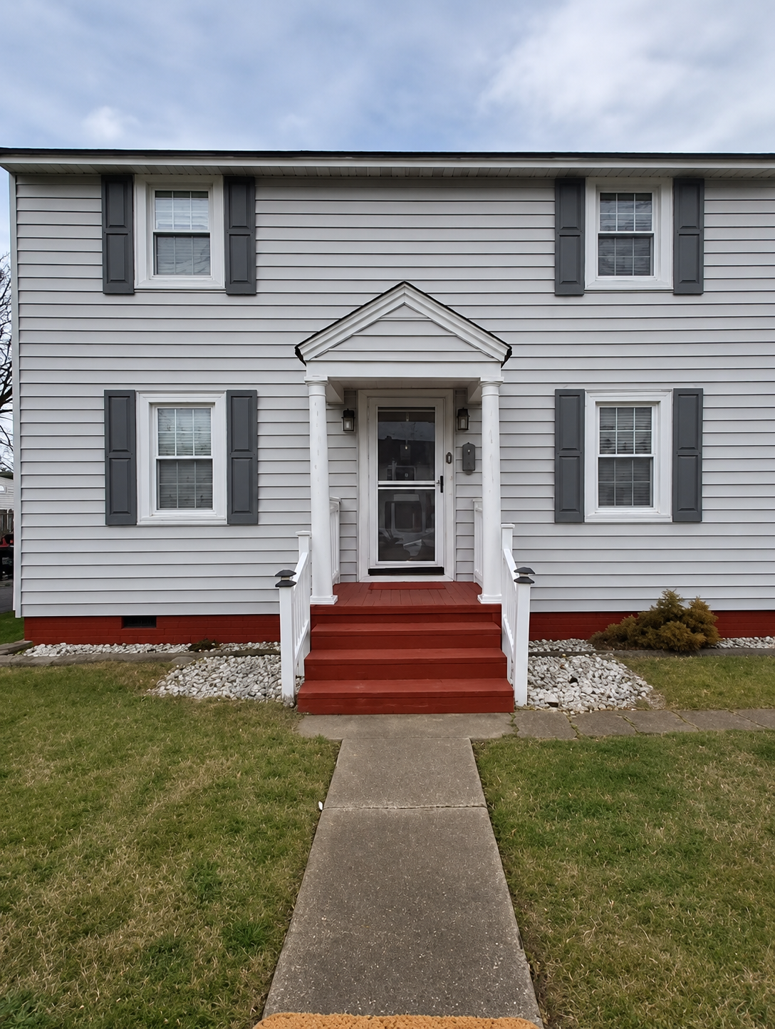 Gray two-story house with red steps and a front walkway leading to the entrance