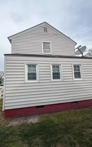 Side view of a white house with gray siding, red foundation trim, and several windows on a grassy lot.