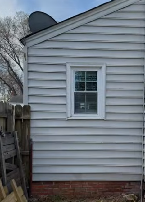 Side of a white house with a small window, brick foundation, and a fence on the left side.