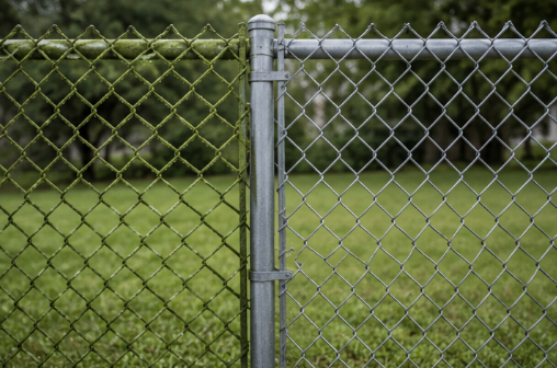 Chain-link fence with a metal post in front of a green grassy yard and trees