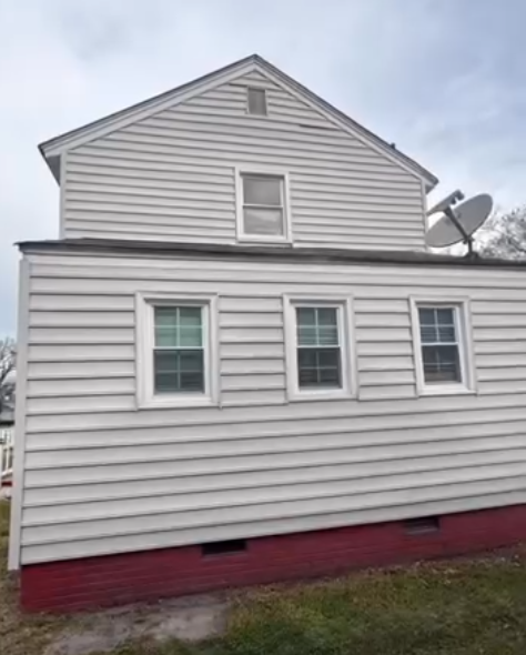 White house exterior with gray siding, three windows, and a red foundation trim