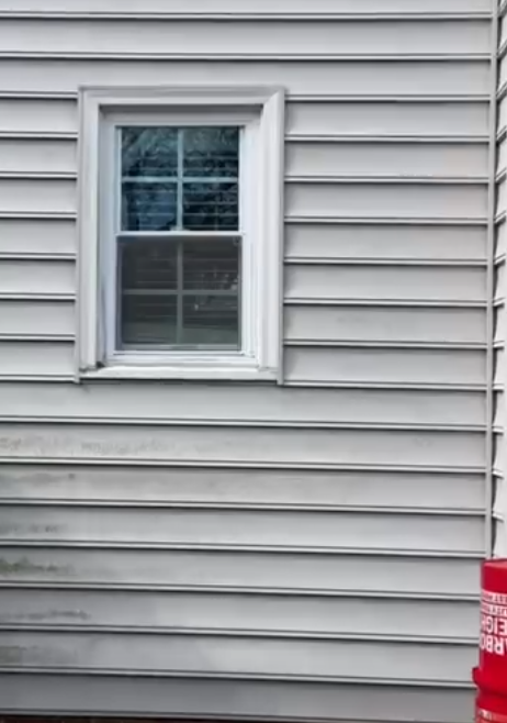 White-framed window on gray vinyl siding; partial red object at bottom right.