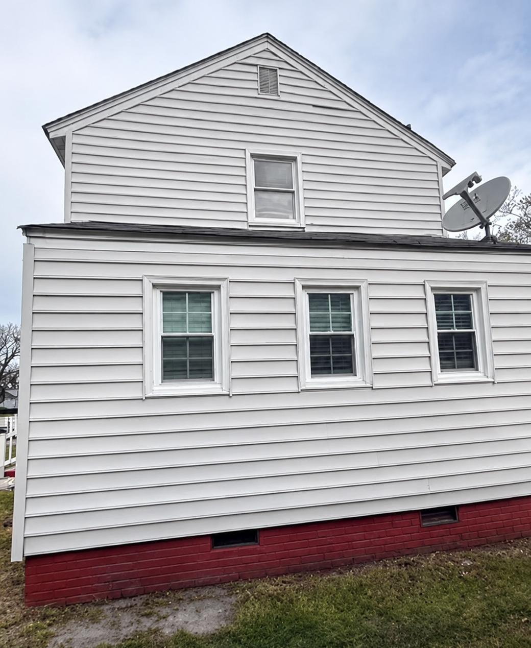 White clapboard house with a red foundation and two satellite dishes on the side.