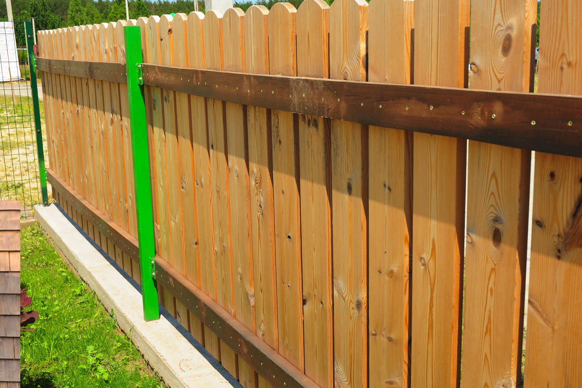 Wooden backyard fence with a bright green post and brick edging along the base.