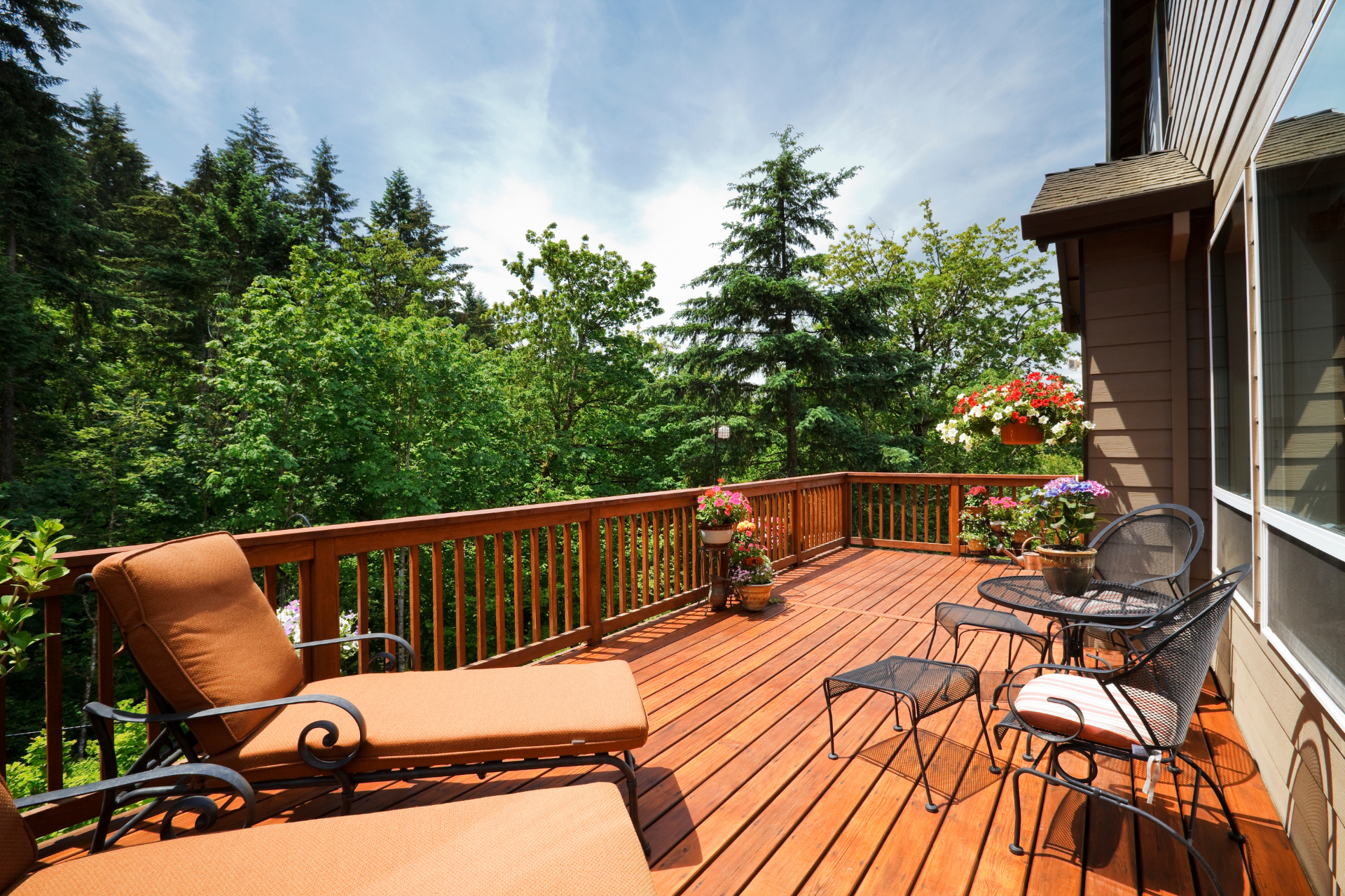 Sunny wooden deck with lounge chairs and a small table overlooking trees and greenery