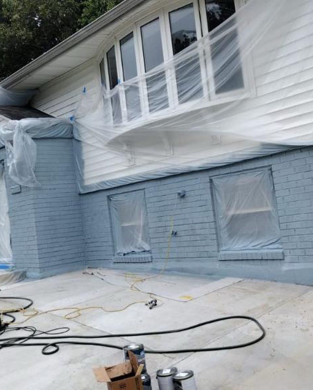 A house is being painted blue and white and is covered in plastic.