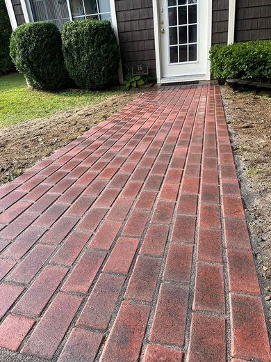 A red brick walkway leading to a house with a white door.