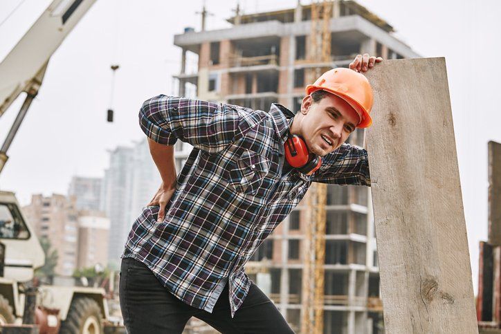 Hard work. Construction worker in protective helmet feeling back pain while working at construction site.