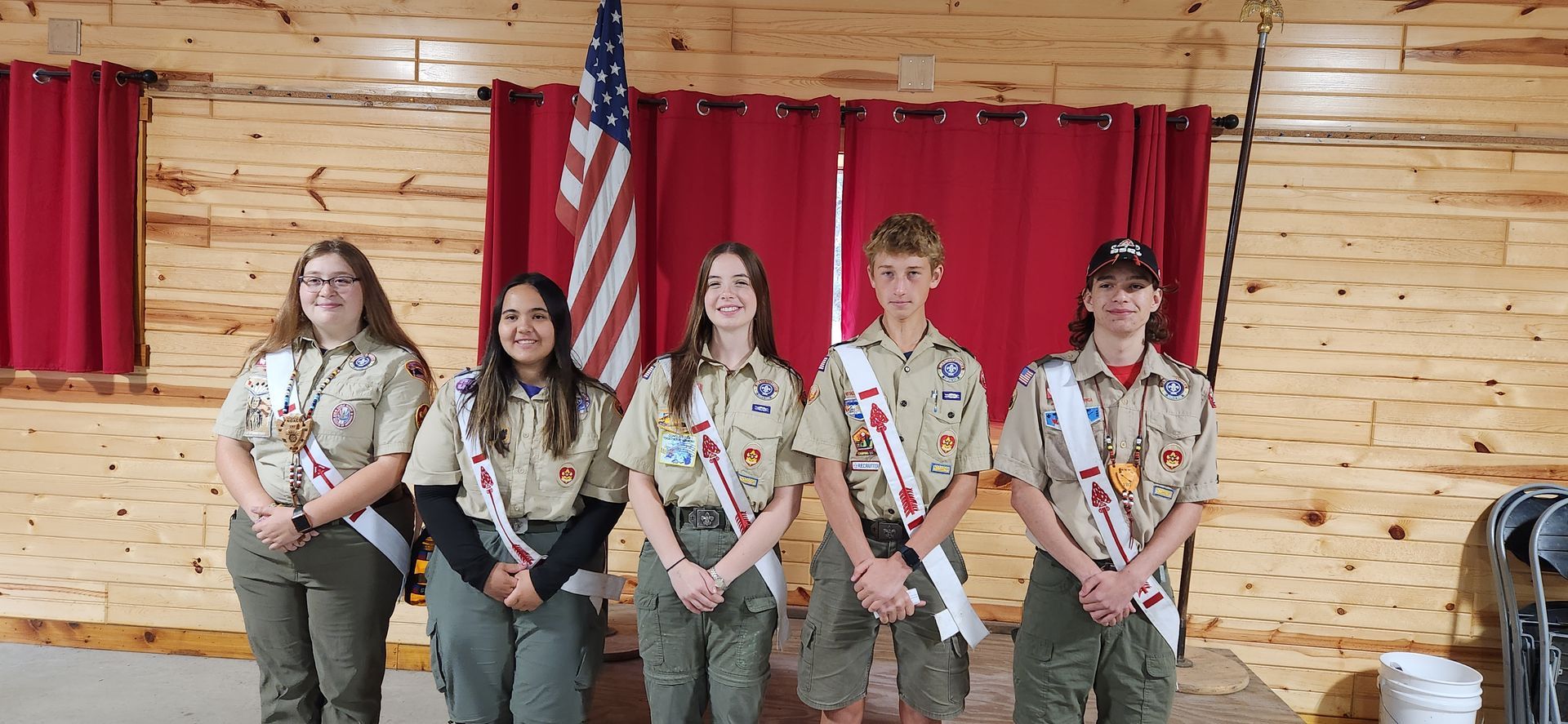 A group of boy scouts are posing for a picture in front of an american flag.