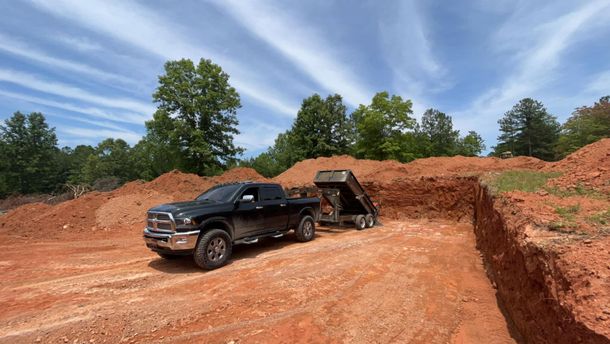 A black truck is parked in a dirt field next to a pile of dirt.