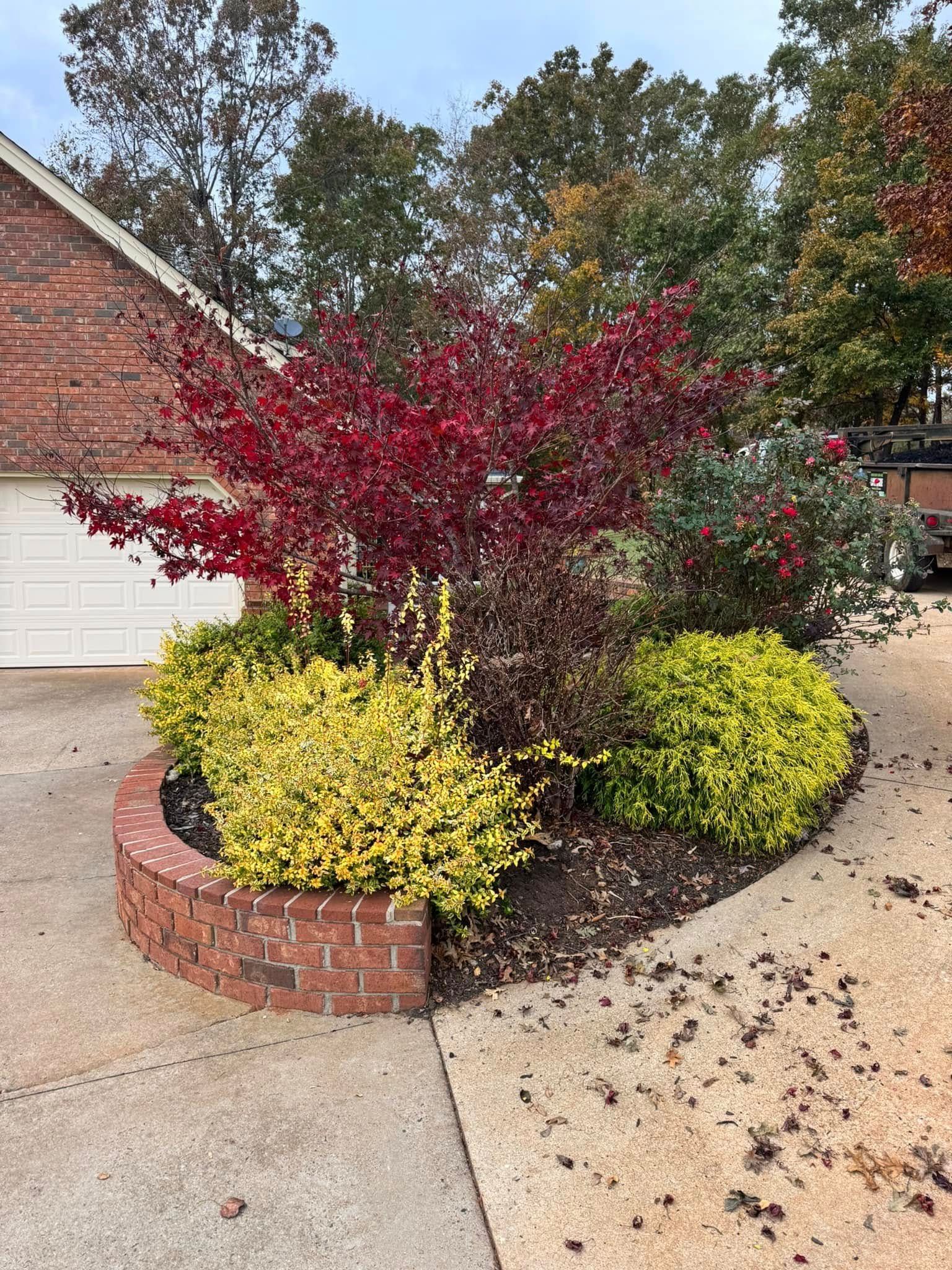 A brick planter with a tree in the middle of it in front of a house.