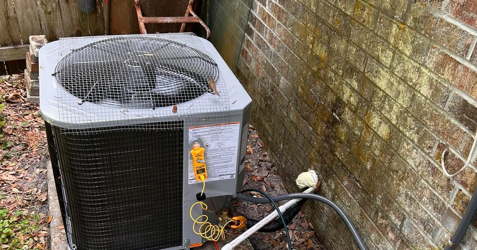 Air conditioning unit next to a brick wall with water stains.