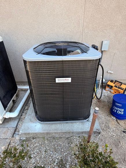 Air conditioner unit against a light-colored wall, with a small blue bucket and tools visible nearby.