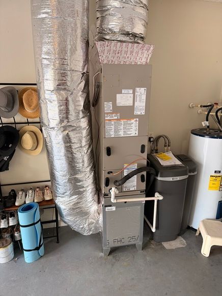 Furnace and water softener in a garage, next to a water heater. Ductwork and hats are also visible.