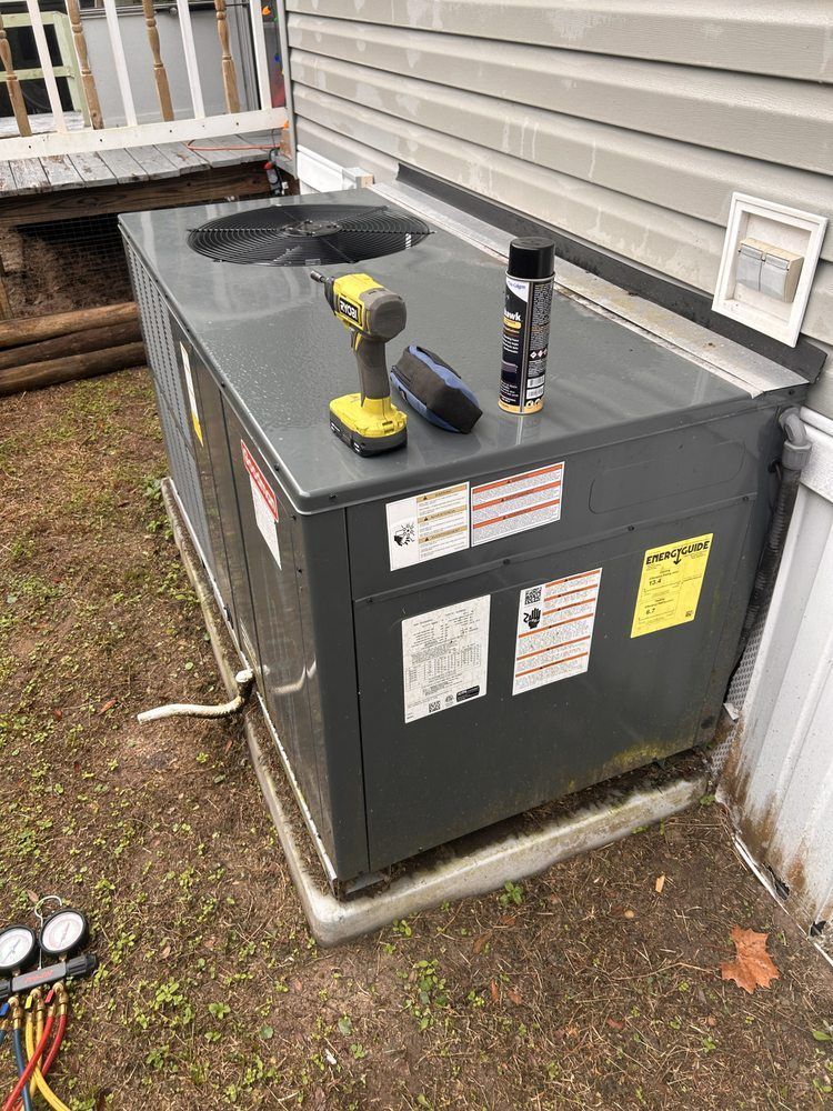 An air conditioning unit on concrete base; tools and spray can on top. Gray siding in the background.