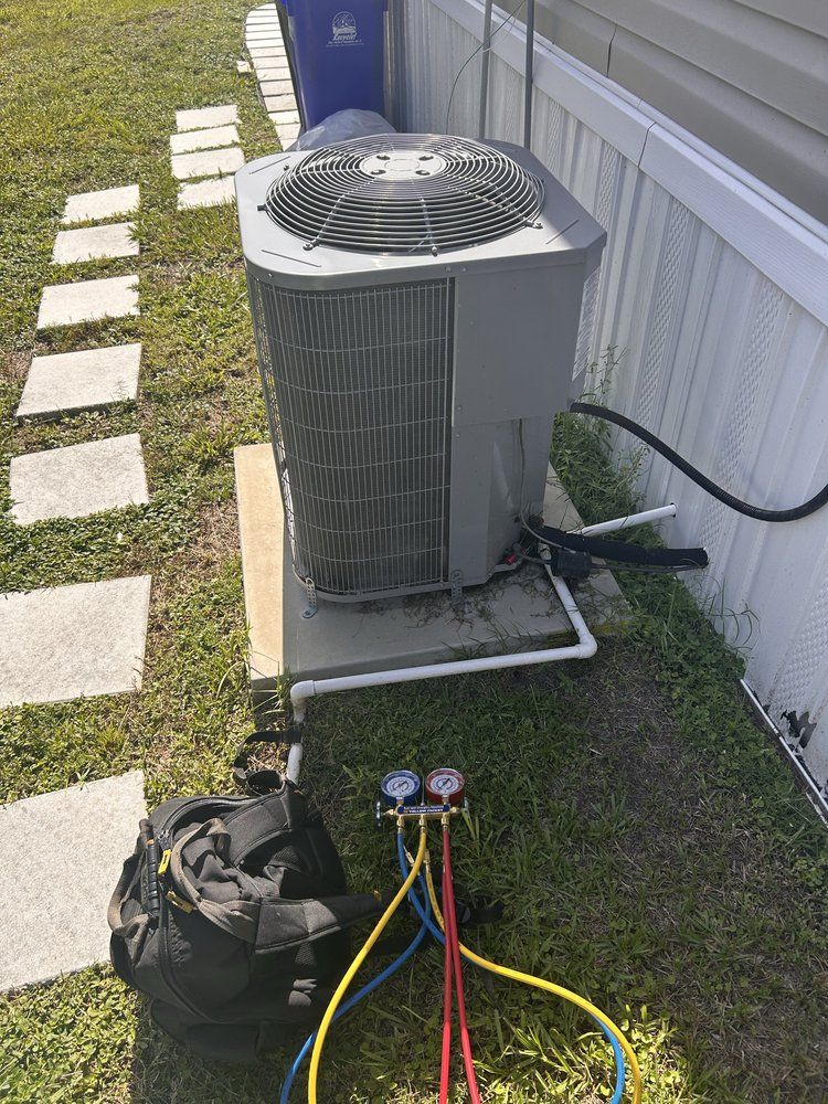 HVAC unit with gauges, next to a building and trash can, on a concrete pad, outdoors on grass.