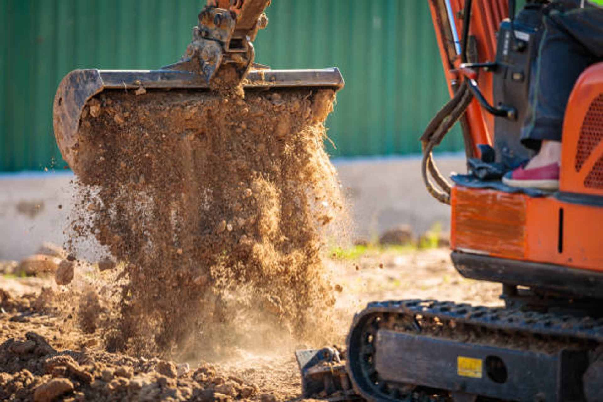 Hole dug in grass, red soil pile, brick, green hose, shovel.