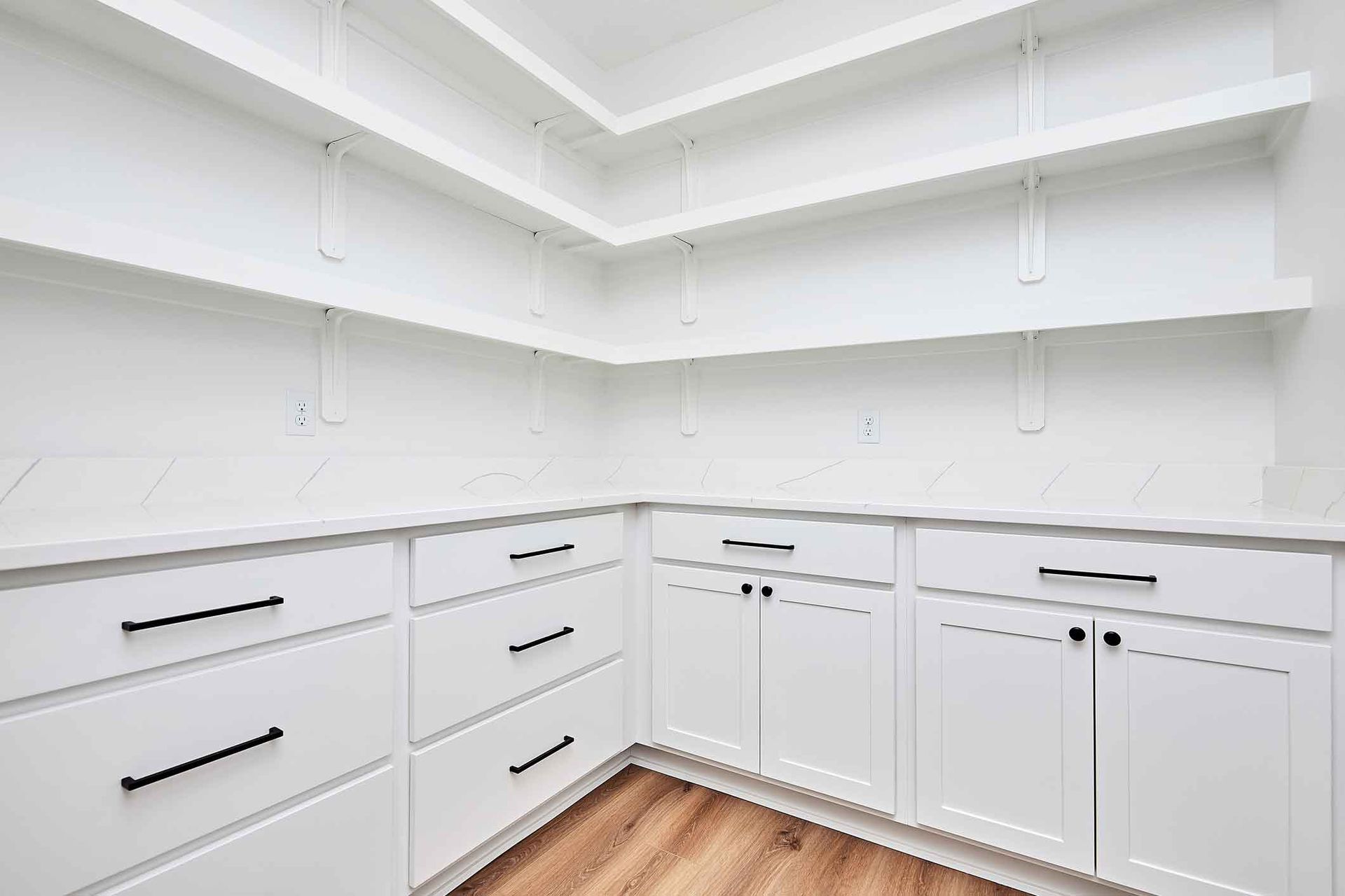 A kitchen with white cabinets , drawers , and shelves.