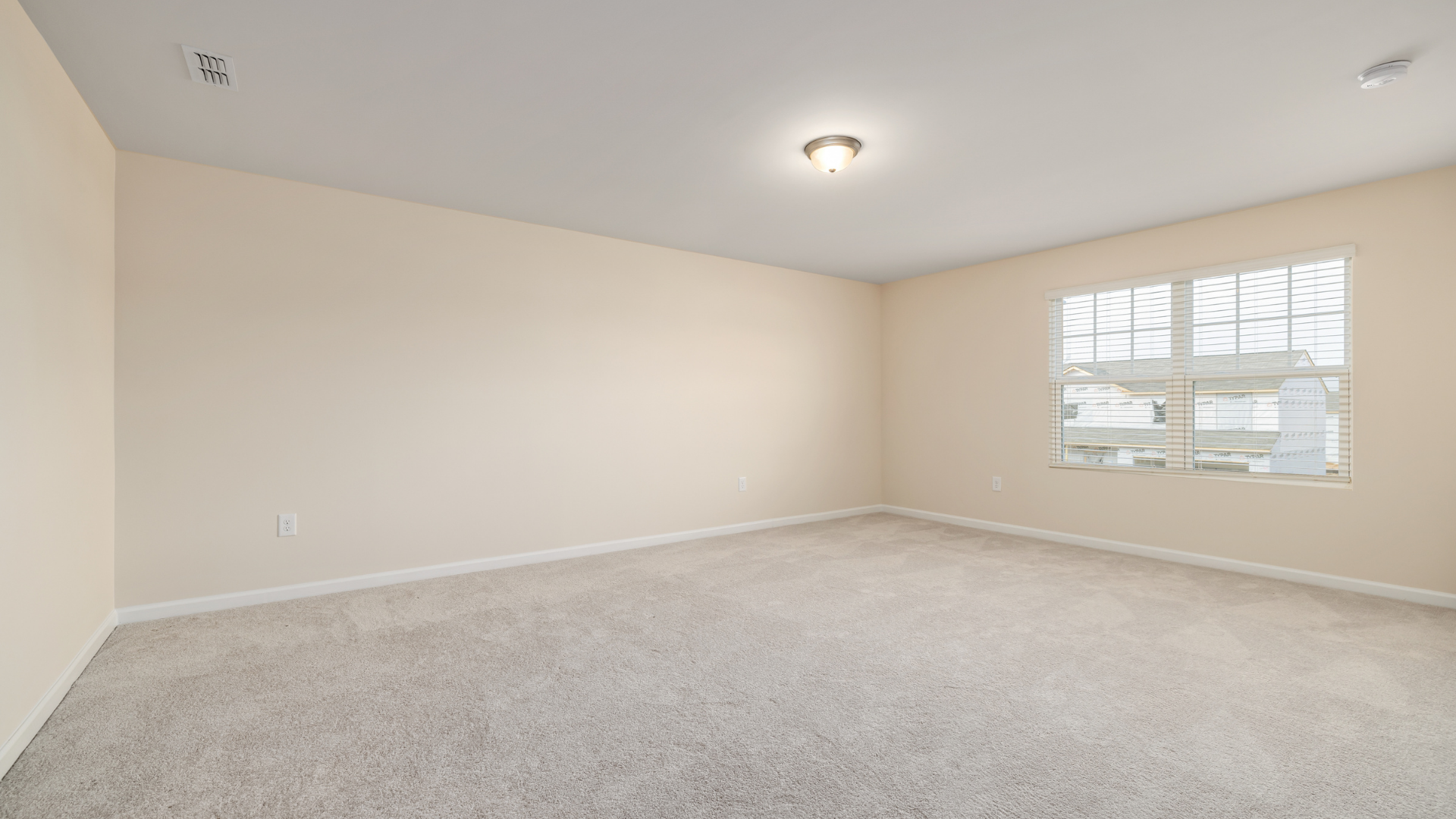 Empty room with beige walls, white trim, light gray carpet, and a window.