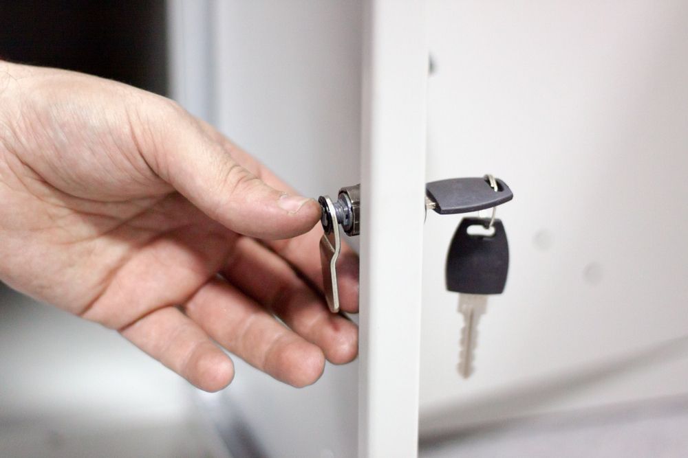 Hand Turning a Key in A White Cabinet Lock — CQR Locksmiths in Moree, NSW