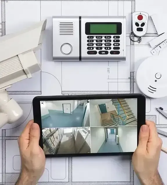 Hands Holding A Tablet Showing Security Camera Feeds Over A Blueprint With Alarm, Cameras — CQR Locksmiths In Moree, NSW