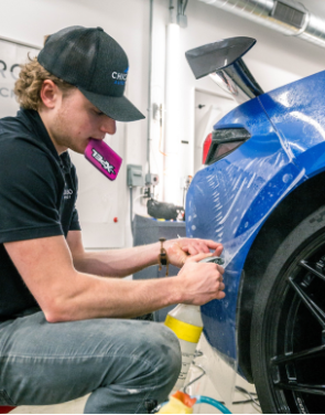A man in a black hat is working on a blue car