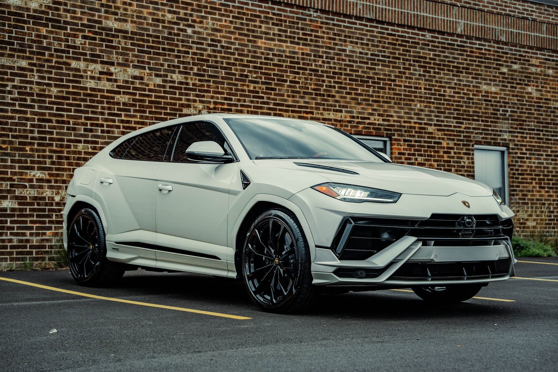 A white lamborghini urus is parked in front of a brick building.
