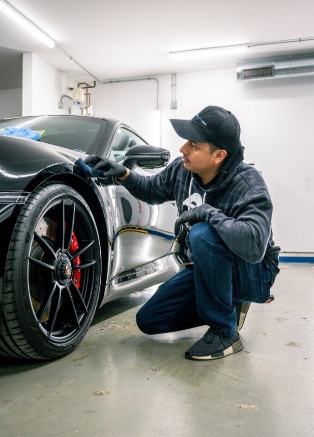 A man is kneeling down next to a sports car in a garage.