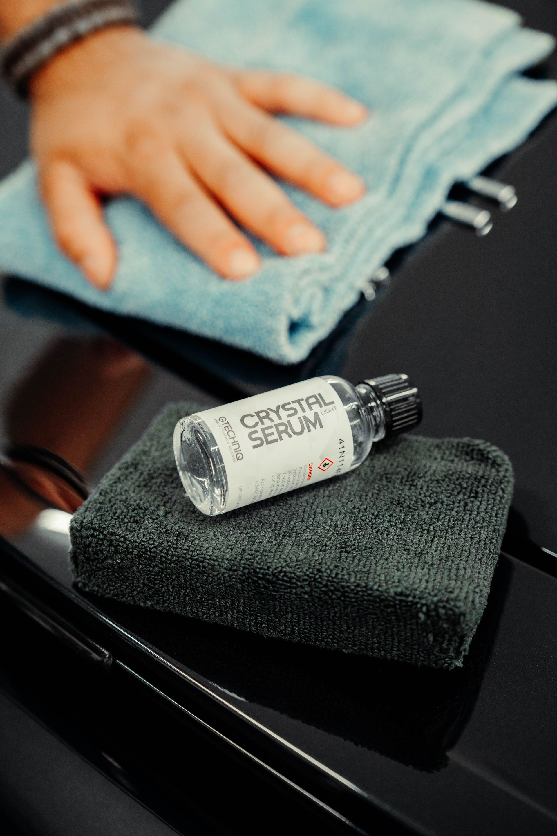 A person is cleaning a car with a towel and a bottle of crystal serum