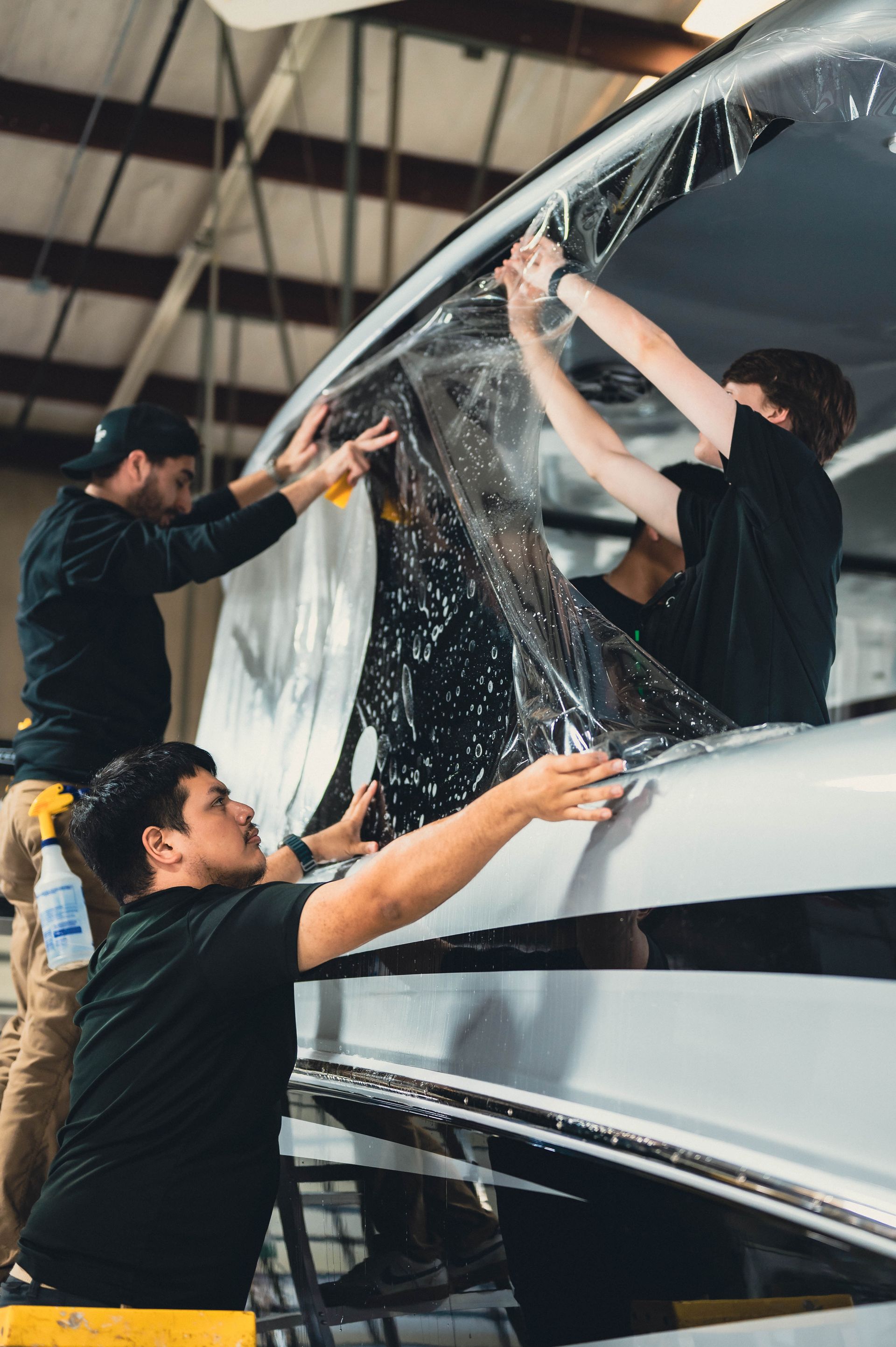 Two men are wrapping a car in plastic.