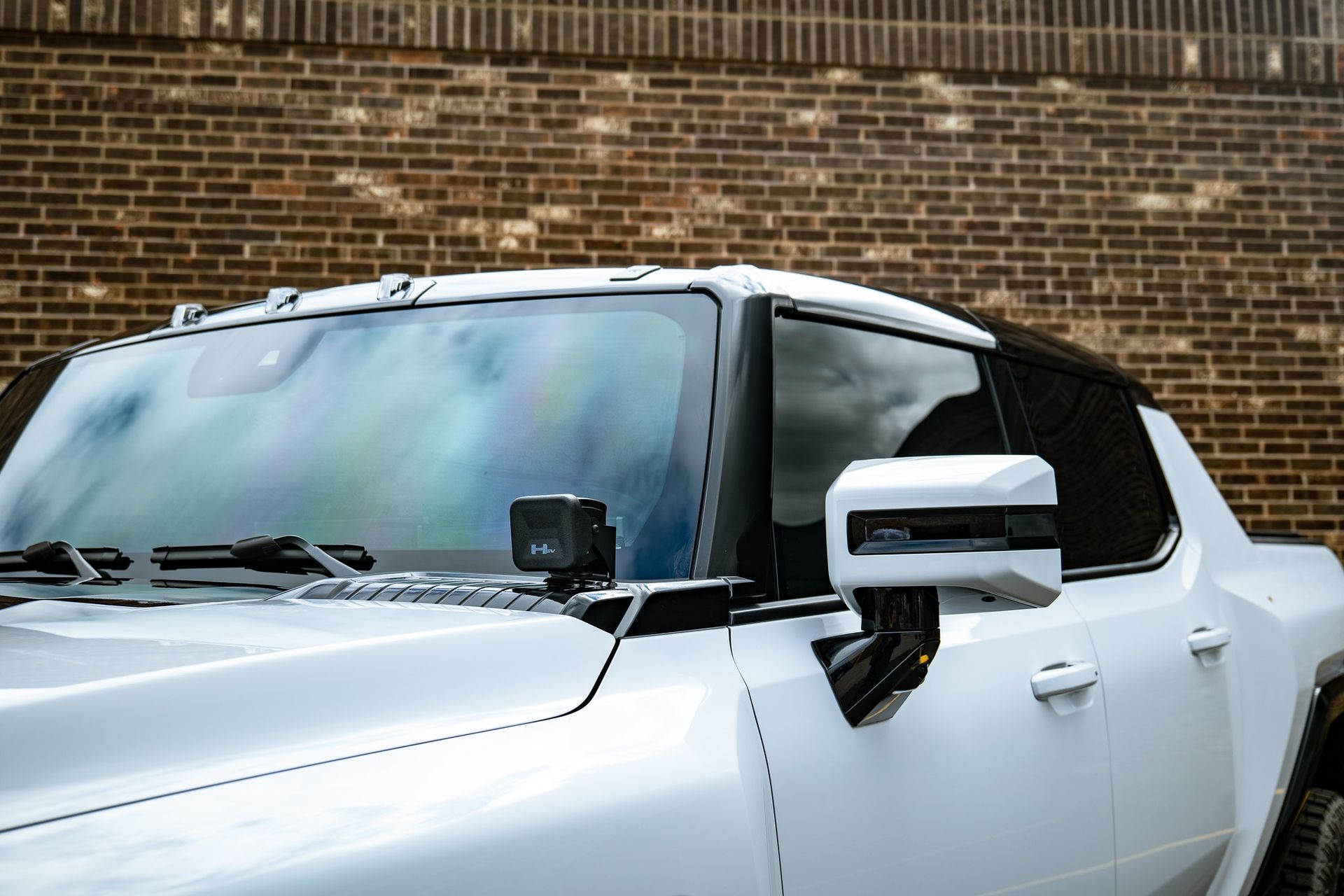 A white hummer truck is parked in front of a brick wall.