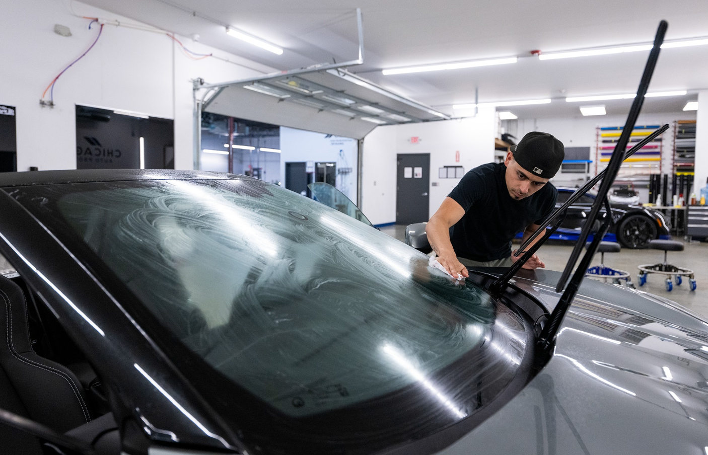A man is cleaning the windshield of a car in a garage.