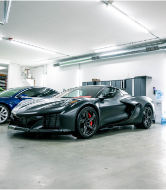 A black sports car is parked in a garage next to a blue sports car.